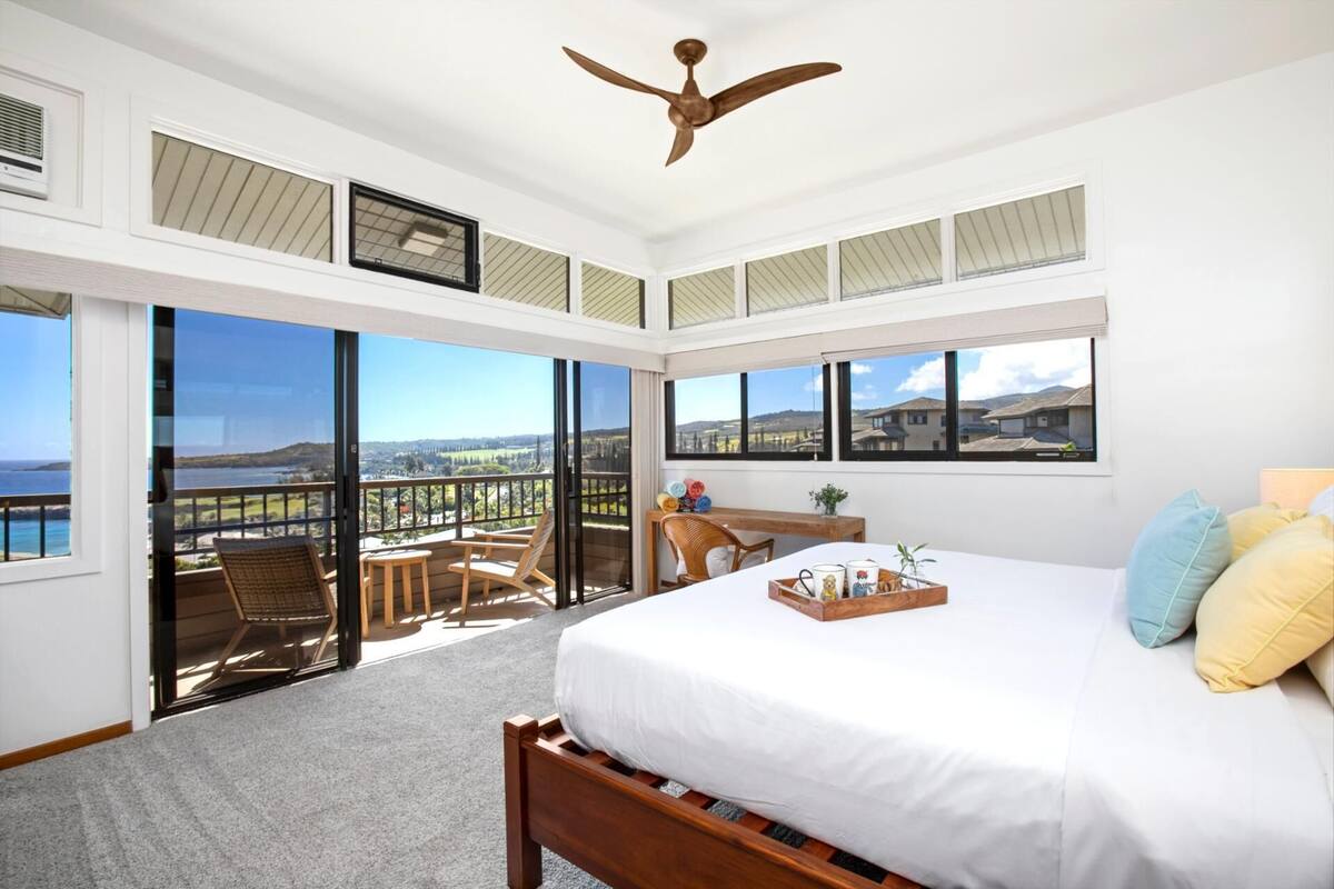 A bedroom with a large bed, a ceiling fan, and a balcony with a view.
