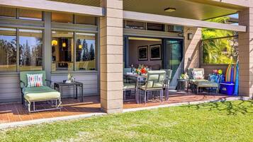 A covered patio with outdoor seating, a dining table, and a small garden area.