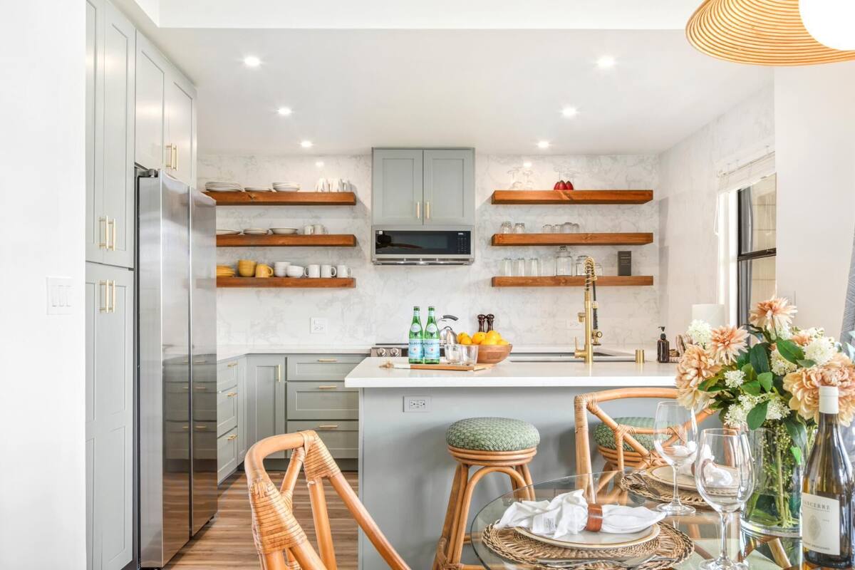 A modern kitchen with grey cabinets, wooden shelves, and a central island.
