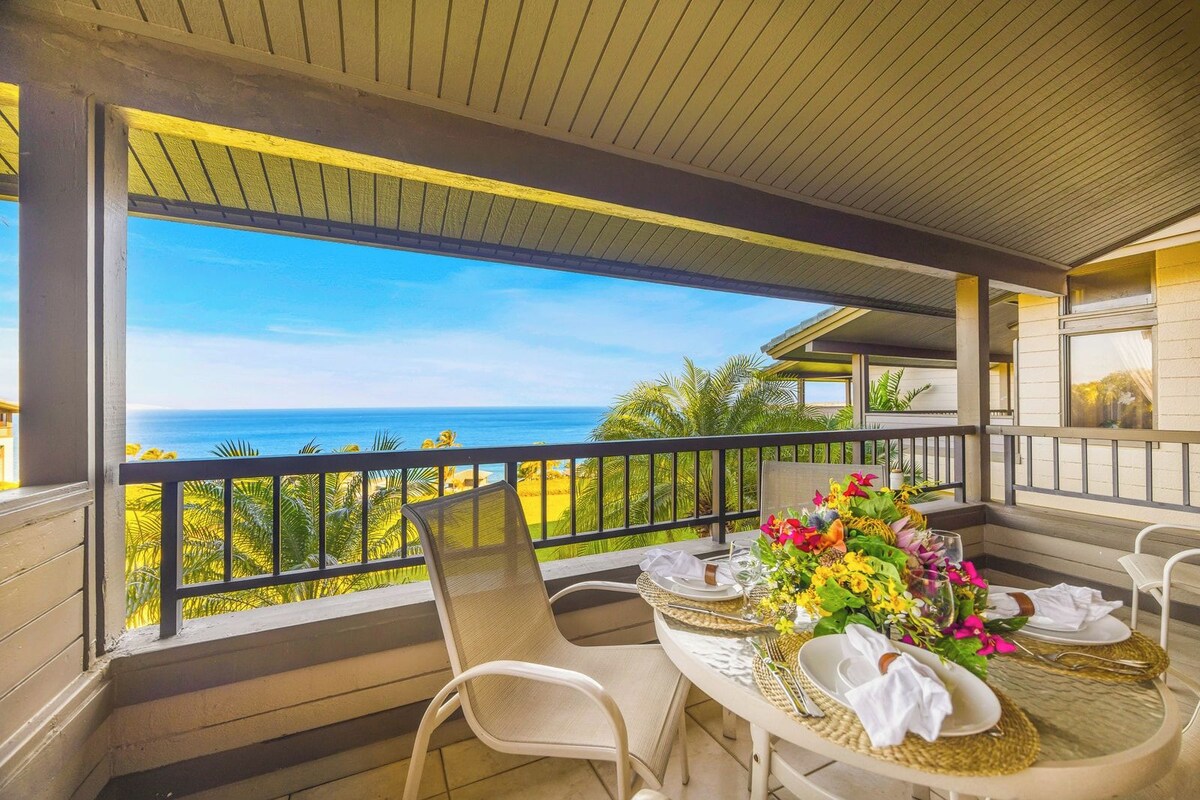 A covered outdoor dining area with a view of the ocean, a table set for two, and a chair.