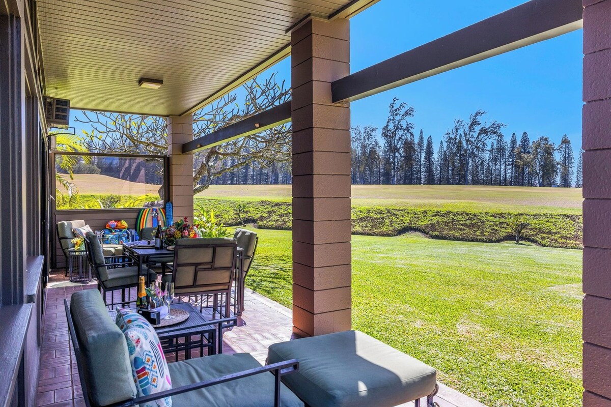 A covered patio with outdoor furniture, a table set with drinks, and a view of a golf course.