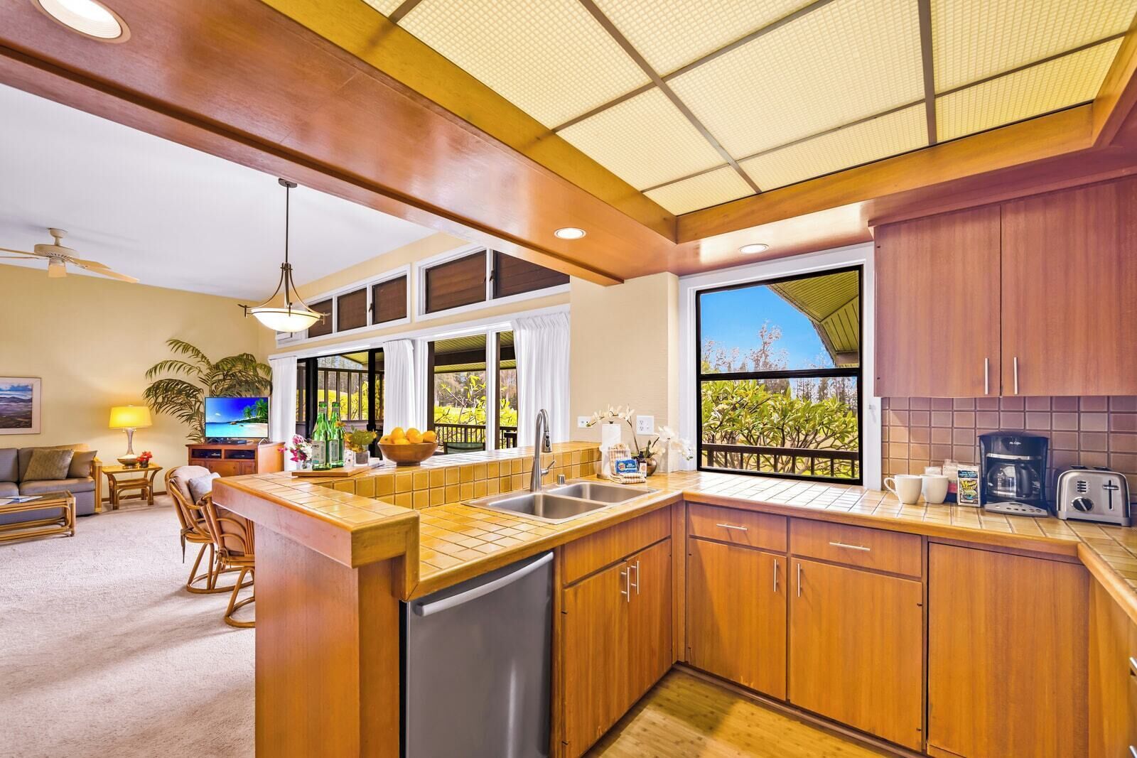 A modern kitchen with wooden cabinets, a stainless steel sink, and a large window offering a view of greenery.