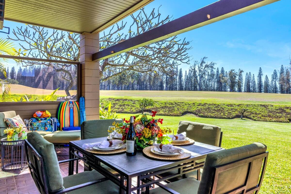 A covered outdoor dining area with a table set for two, chairs, and a view of a golf course.