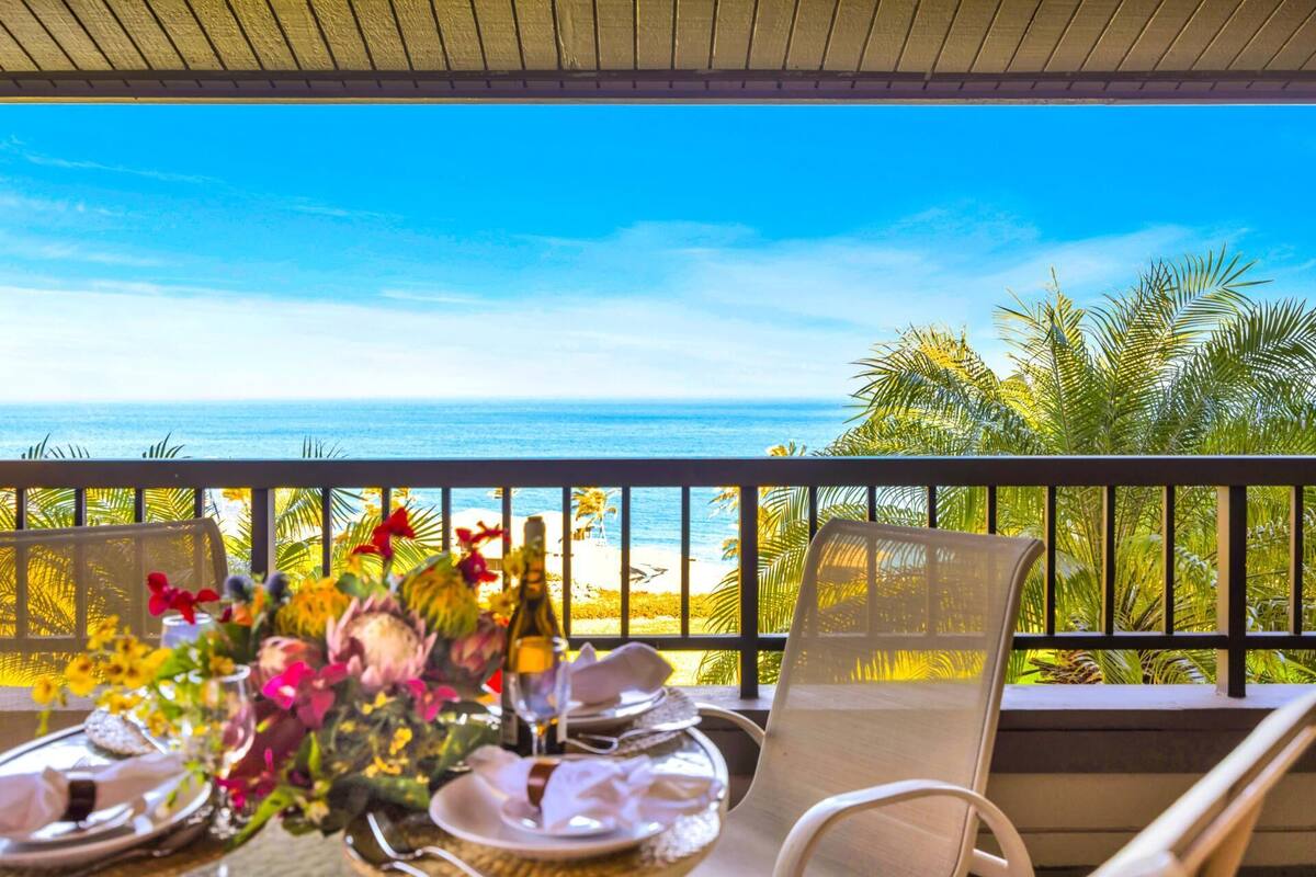 A balcony with a table set for two, overlooking a beach and ocean.