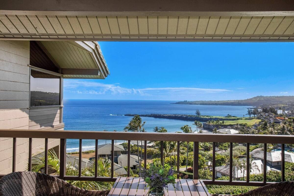 A balcony with a view of the ocean, a wooden deck, and a building with a sloped roof.