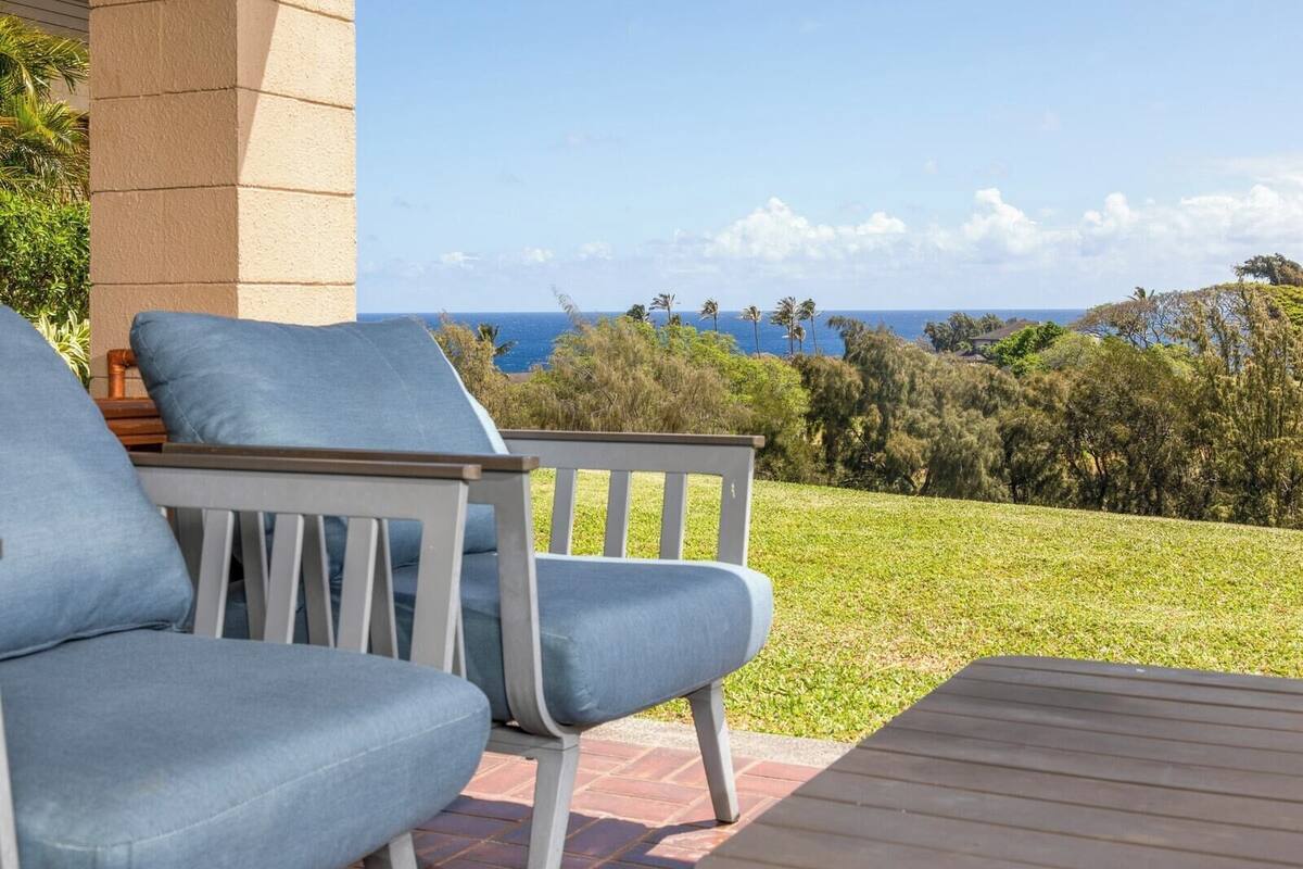 A patio with two chairs and a table, overlooking a grassy area and the ocean.