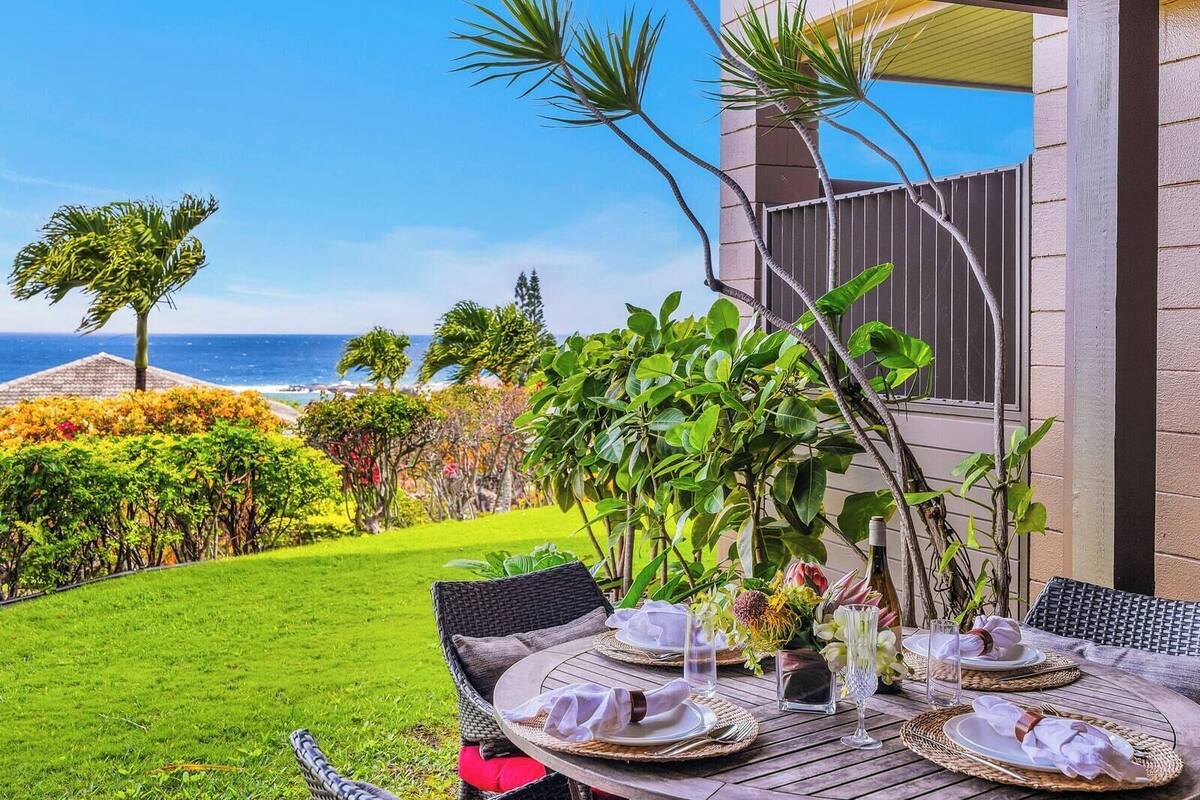 A dining table set outdoors with a view of the ocean.
