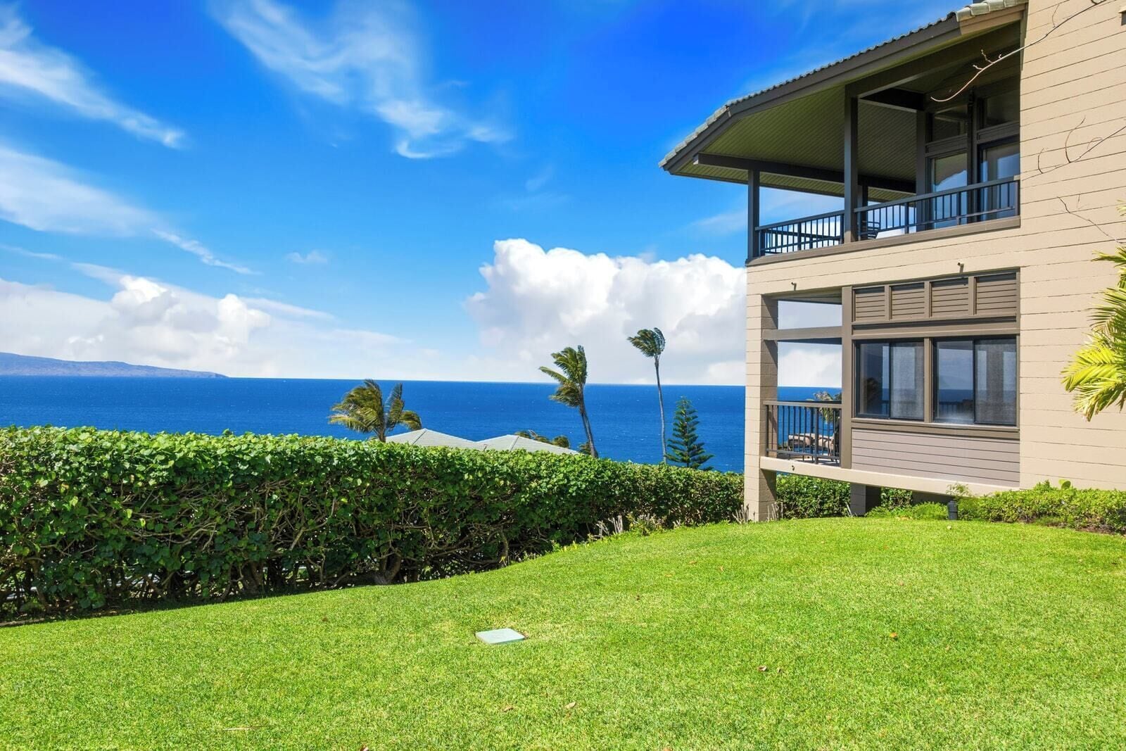 A modern two-story building with a balcony overlooking a grassy area and a view of the ocean.
