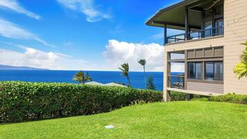 A modern two-story building with a balcony overlooking a grassy area and a view of the ocean.