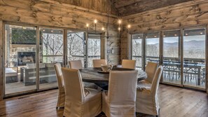 Un intérieur en bois avec une table ronde et des chaises, de grandes fenêtres et une cheminée.