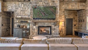 A stone-walled living room with a fireplace, a flat-screen TV, and a sofa. - Changes In Altitude - Mountain Luxury | 4 Master Suites | Panoramic Views (Mineral Bluff)