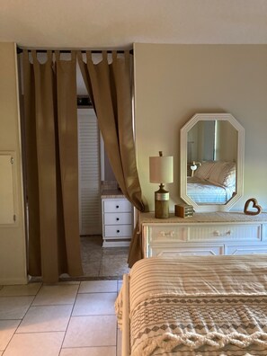 A bedroom with a bed, a dresser, a mirror, and a door with curtains.
