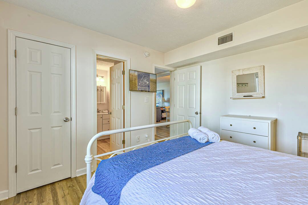 Une chambre à coucher avec un lit, une commode blanche et une porte donnant sur une autre pièce.