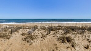 Une plage de sable bordée de clôtures en bois et où la végétation est clairsemée.