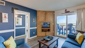 Un salon doté d’un toit en bois à quatre versants, d’un téléviseur et offrant une vue sur la plage grâce à une porte-fenêtre coulissante.