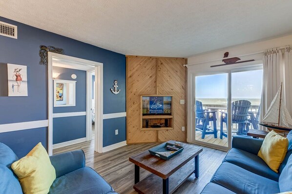 A living room with a wooden hipped roof, a television, and a view of the beach through a sliding glass door. - Oceanfront Escape | Oceanfront | Community Pool (Kill Devil Hills)
