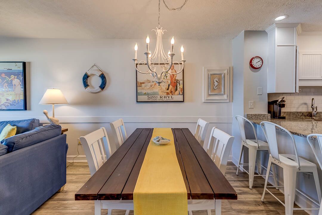 Un comedor con una mesa de madera, sillas blancas y un camino de mesa amarillo.