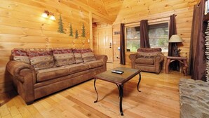 El interior de una cabaña de madera con sofá, sillón y mesa de centro.