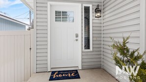 A white front door with a window, a doormat with the text "It's good to be home", and a small potted plant beside the door.