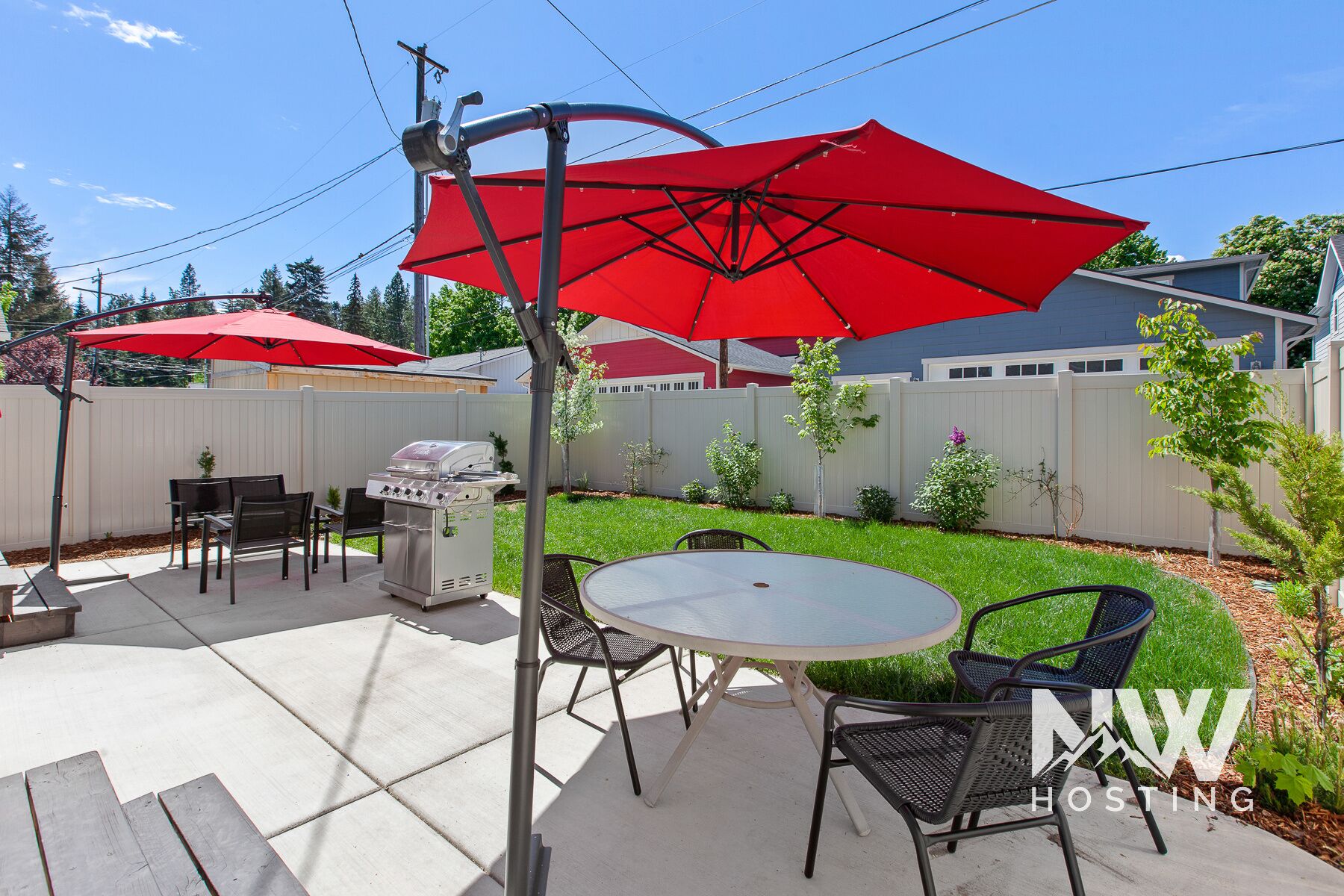 A backyard patio with a grill, outdoor furniture, and red umbrellas.