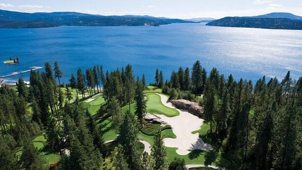 A golf course with a lake view, surrounded by dense forest.