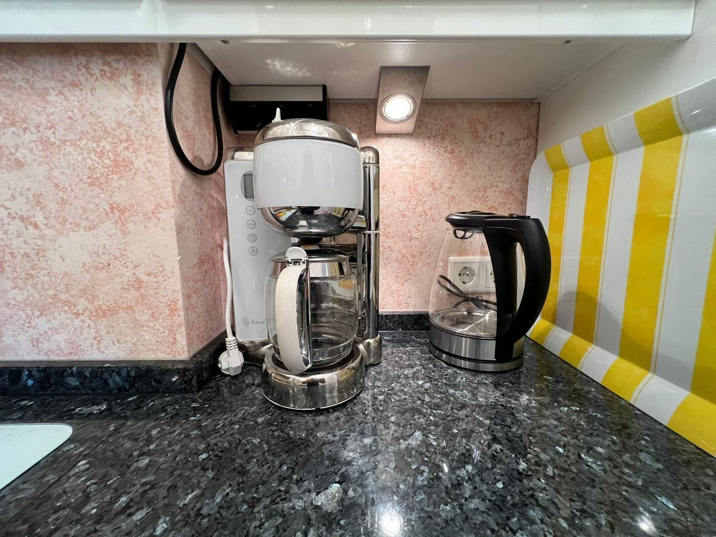 A kitchen with a coffee maker, a kettle, and a microwave.