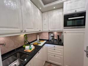 A modern kitchen with white cabinets, a stainless steel sink, a coffee maker, and a microwave. - Sunapp - Individuell Ausgestattetes Appartement (Sylt)