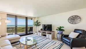 A modern living room with a balcony overlooking the sea, a large wall clock, and a flat-screen TV. - Step into Paradise at South Seas Towers 4-805 (Marco Island)