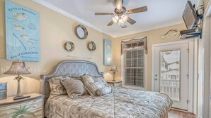 A bedroom with a bed, a ceiling fan, a nightstand, a lamp, a wall clock, and a door. - Tiki Hut W/Tiki Bar|Linens|Golf Cart|Outdoor Area (Myrtle Beach)