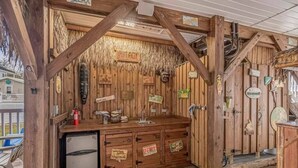 A rustic wooden cabin with a kitchenette, including a refrigerator, sink, and wooden cabinets. - Tiki Hut W/Tiki Bar|Linens|Golf Cart|Outdoor Area (Myrtle Beach)