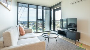 Una sala de estar moderna con un sofá, una mesa de centro, un televisor y grandes ventanas con vista a la ciudad.