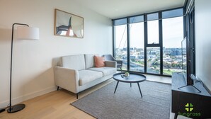 Una sala de estar moderna con un sofá, una mesita de centro y una lámpara de pie. Una ventana grande ofrece vistas de la ciudad.