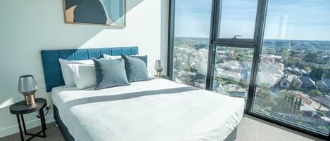 Un dormitorio con una cama grande, vistas a la ciudad y una lámpara moderna.