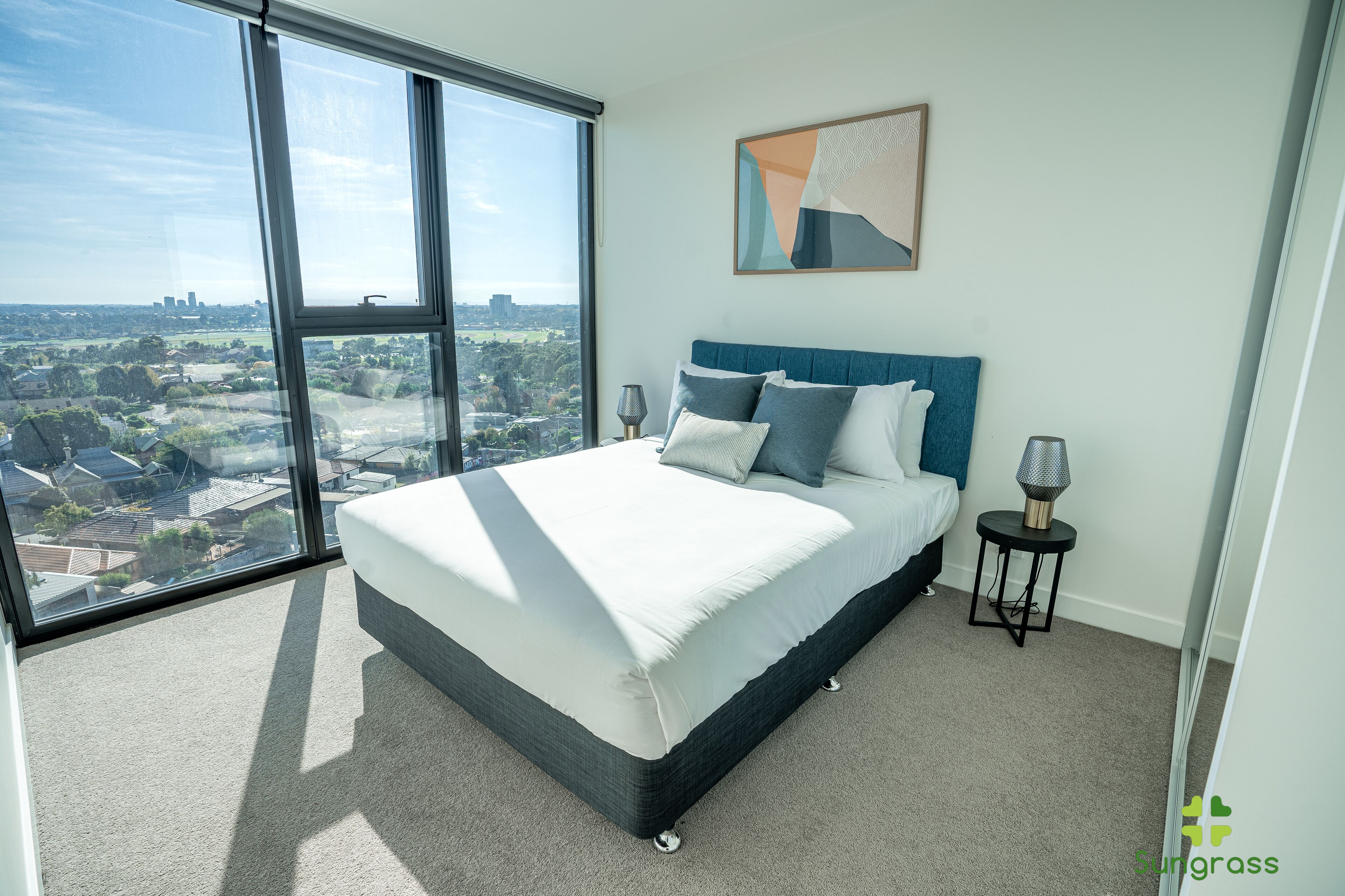 Een moderne slaapkamer met een groot bed, stadszicht en een klein nachtkastje met een lamp.