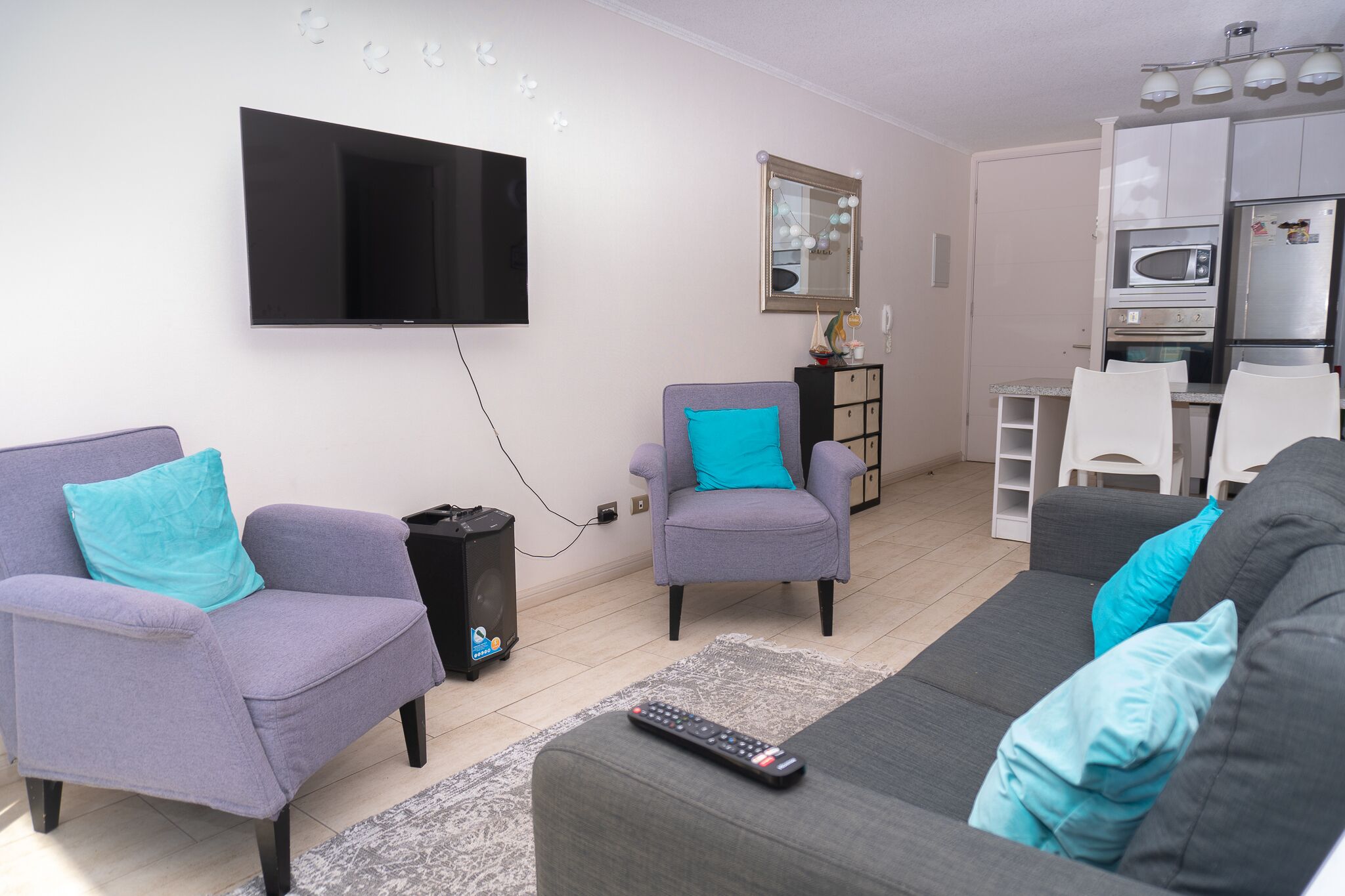 Una sala de estar con un televisor de pantalla plana, dos sillones, un sofá y una zona de cocina al fondo.
