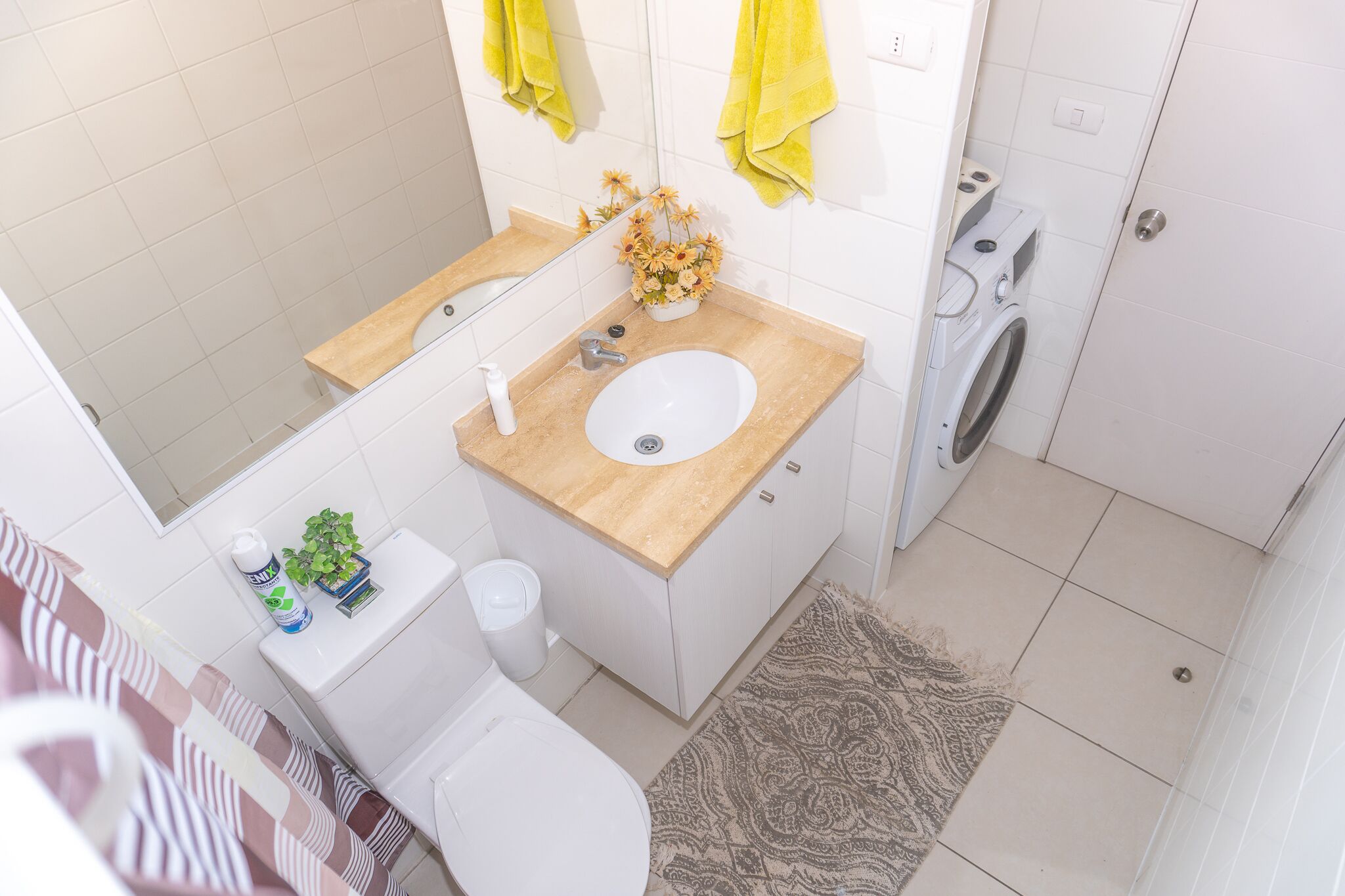 A bathroom with a sink, mirror, toilet, and a washing machine.