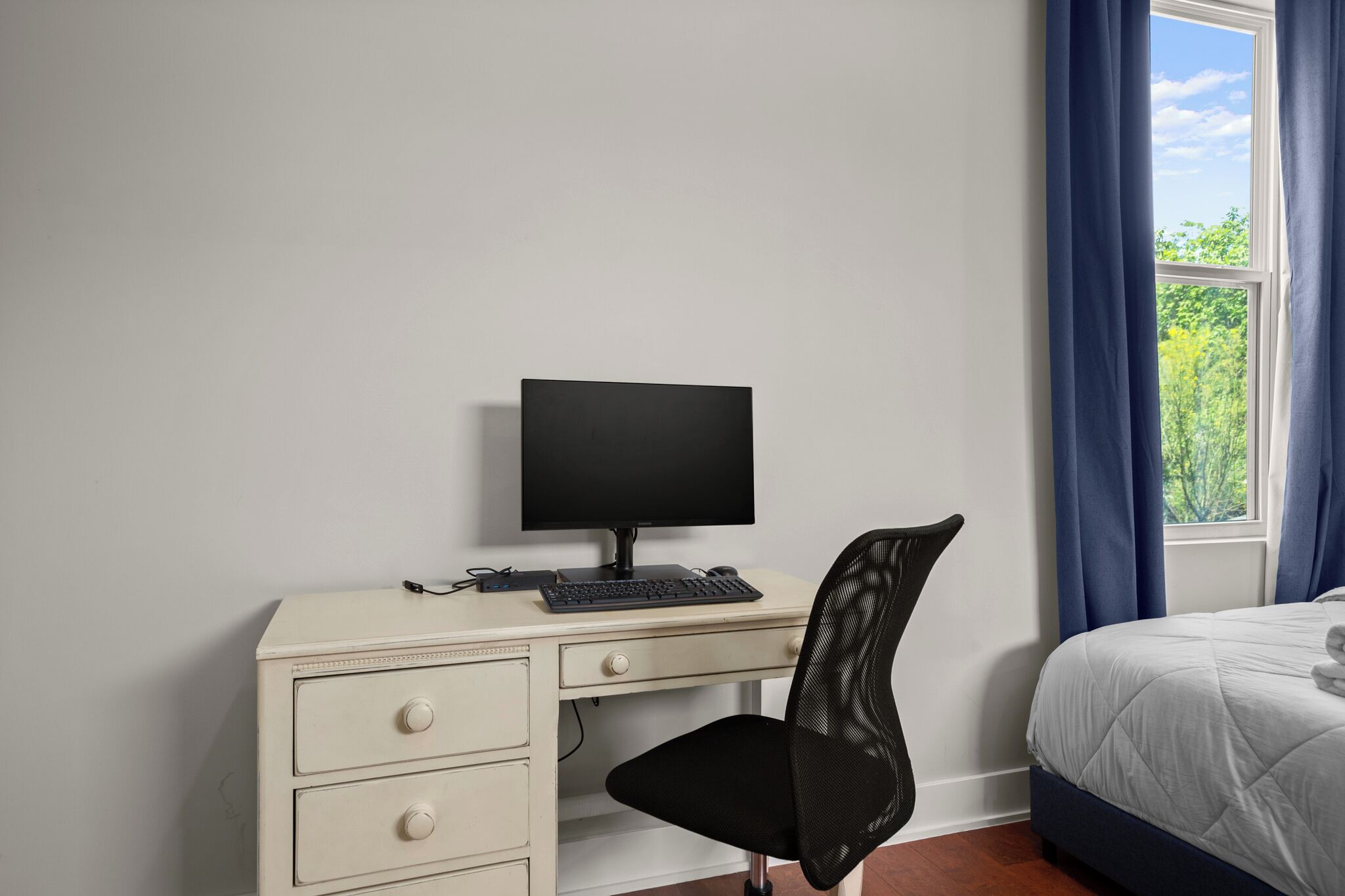 Un dormitorio con una cama, un escritorio con una computadora, una silla y una ventana con cortinas.