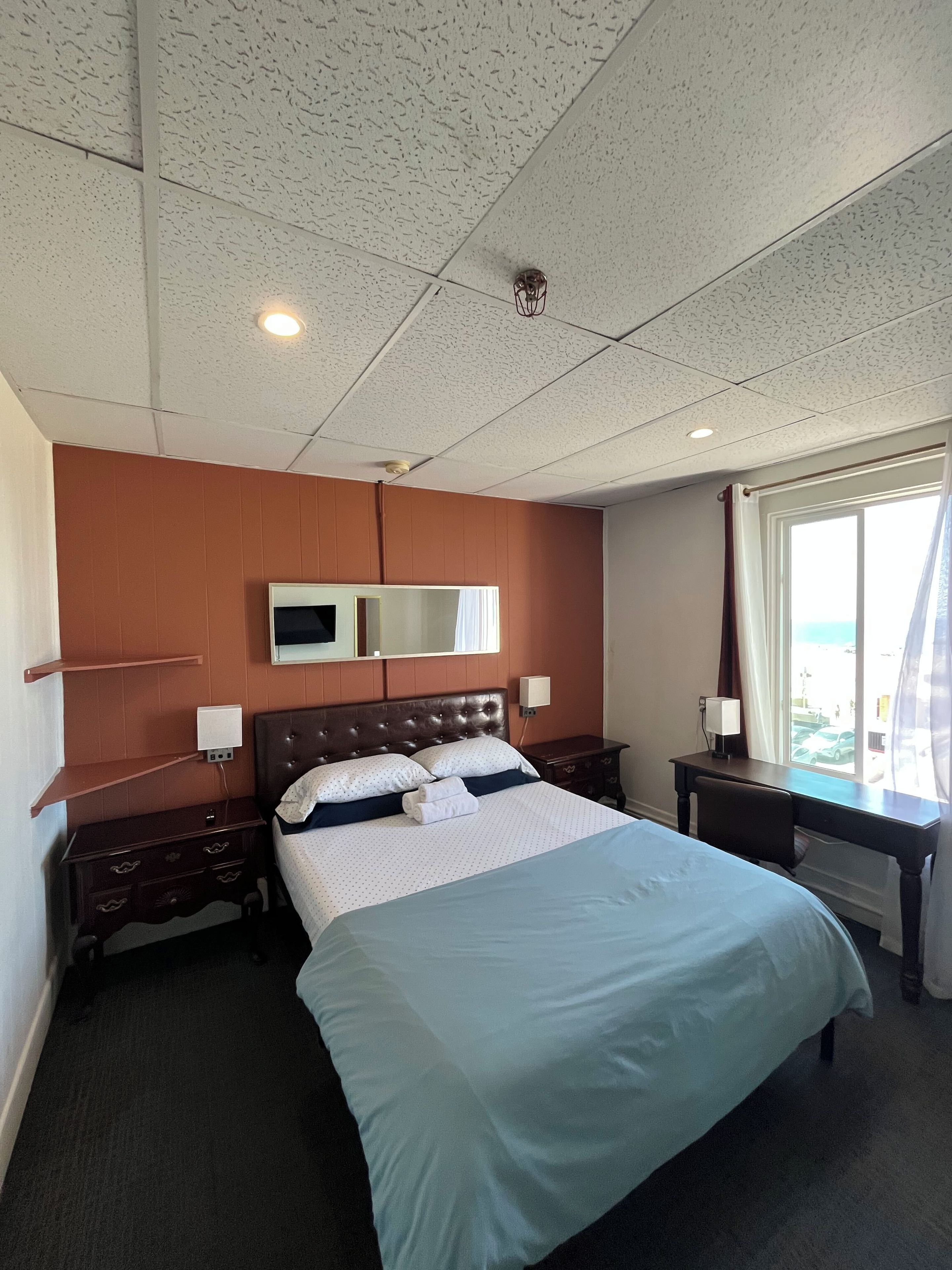 A hotel room with a large bed, a desk, a chair, a TV, and a window with curtains.