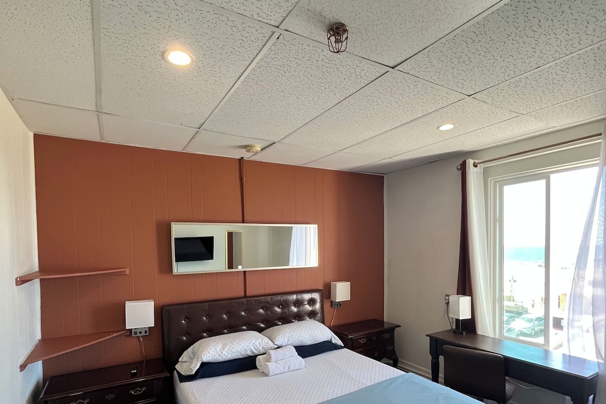 A hotel room with a large bed, a desk, a chair, a TV, and a window with curtains.