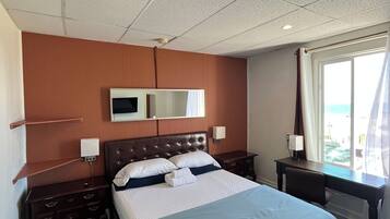 A hotel room with a large bed, a desk, a chair, a TV, and a window with curtains.