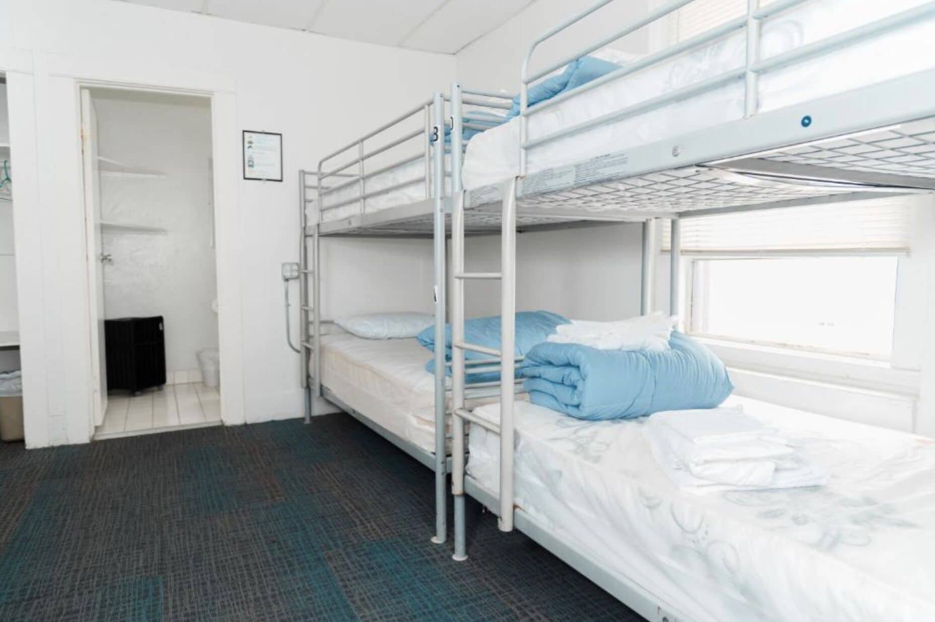 Habitación con literas, puerta a un baño, un radiador y una ventana.