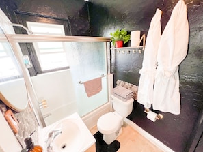 Een badkamer met douche, toilet, wastafel en een handdoekrek met handdoeken.