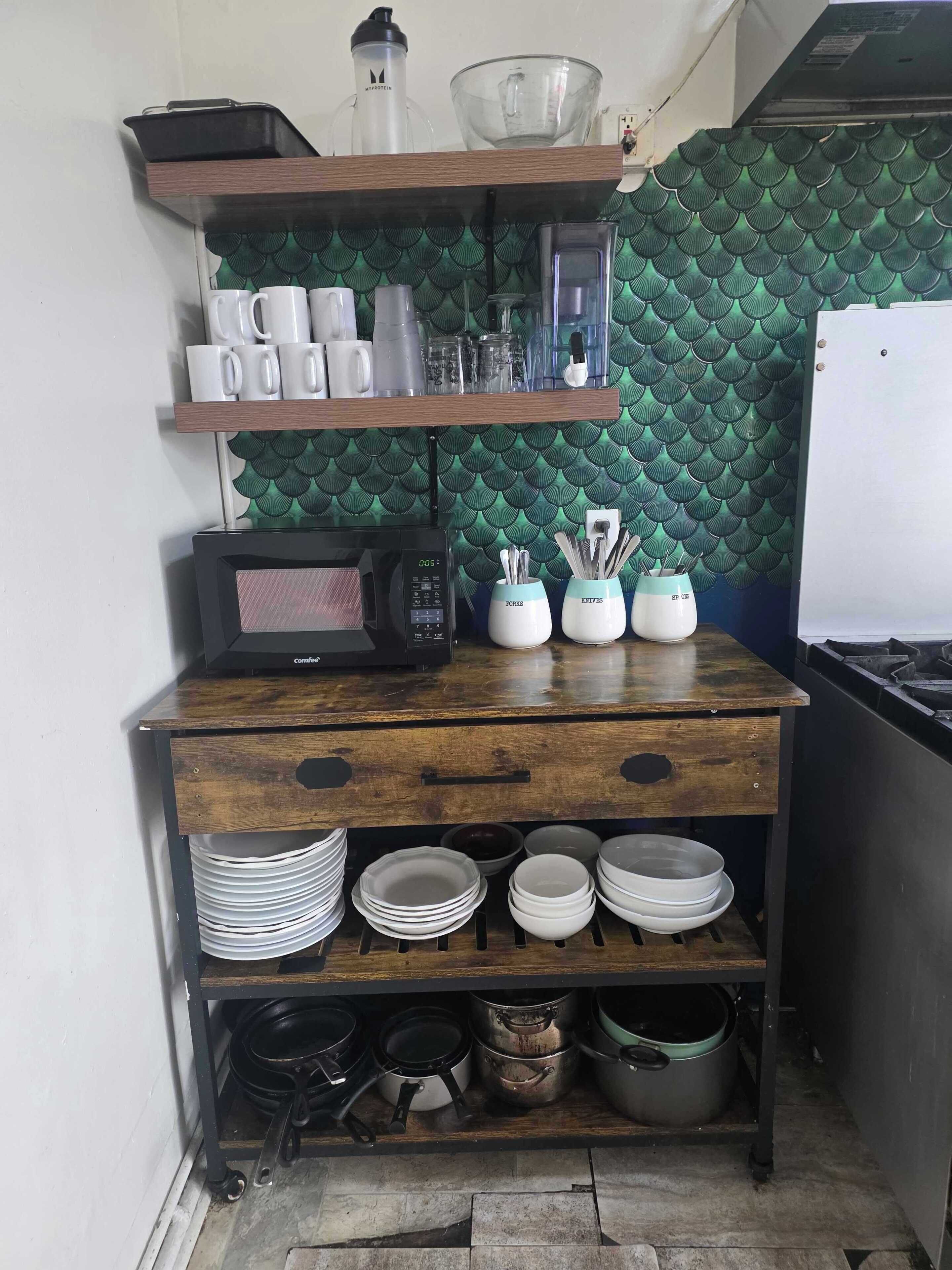 A kitchen with a microwave, coffee maker, and various utensils on a wooden shelf.