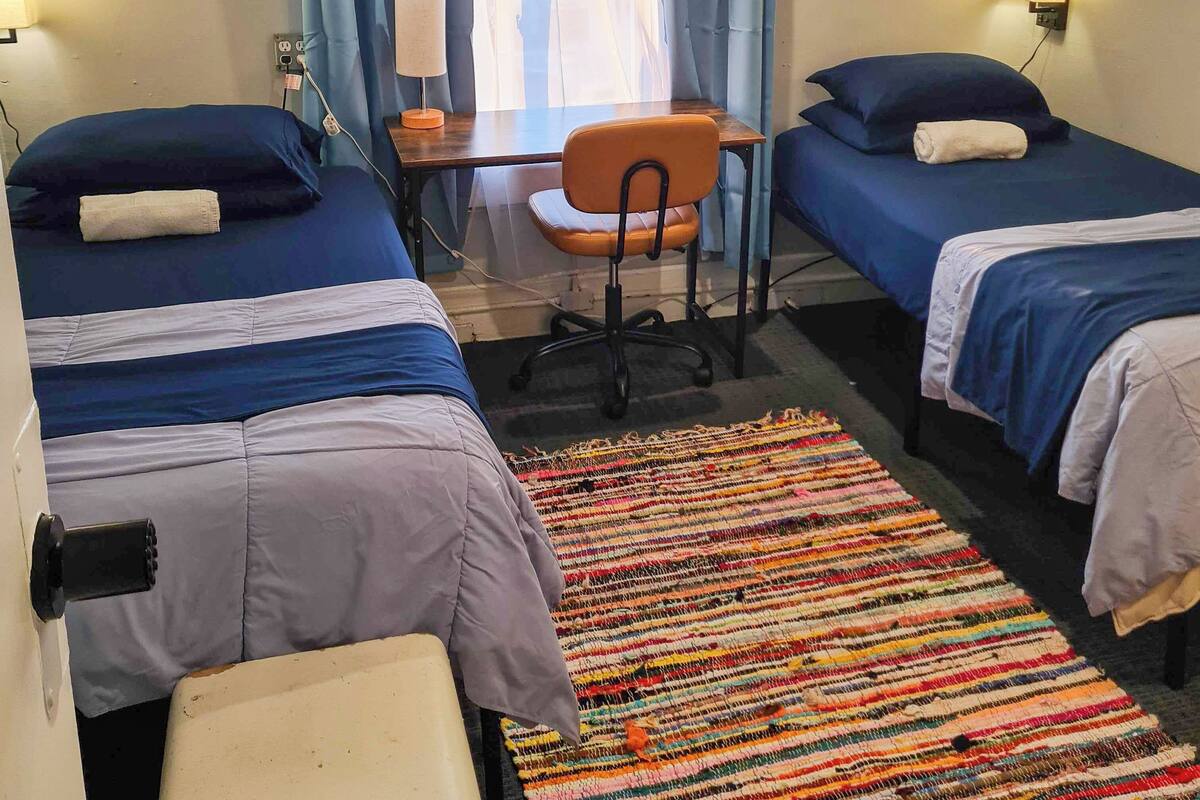 Une chambre avec deux lits, un bureau, une chaise et un tapis coloré.