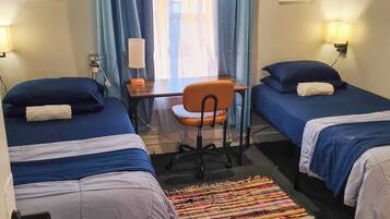 Ein Zimmer mit zwei Betten, einem Schreibtisch, einem Stuhl und einem farbenfrohen Teppich.