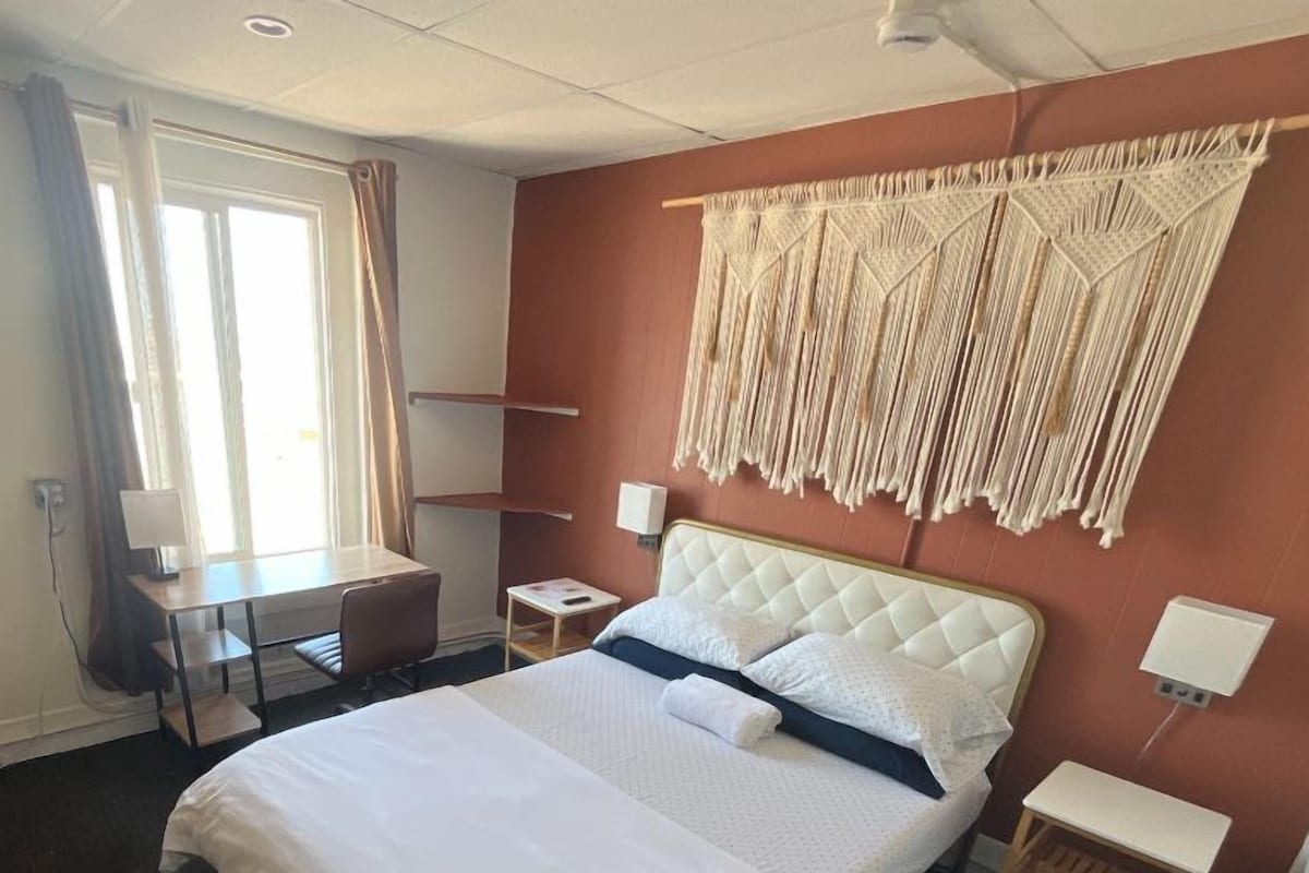 A hotel room with a bed, bedside tables, a desk, and a window with curtains.