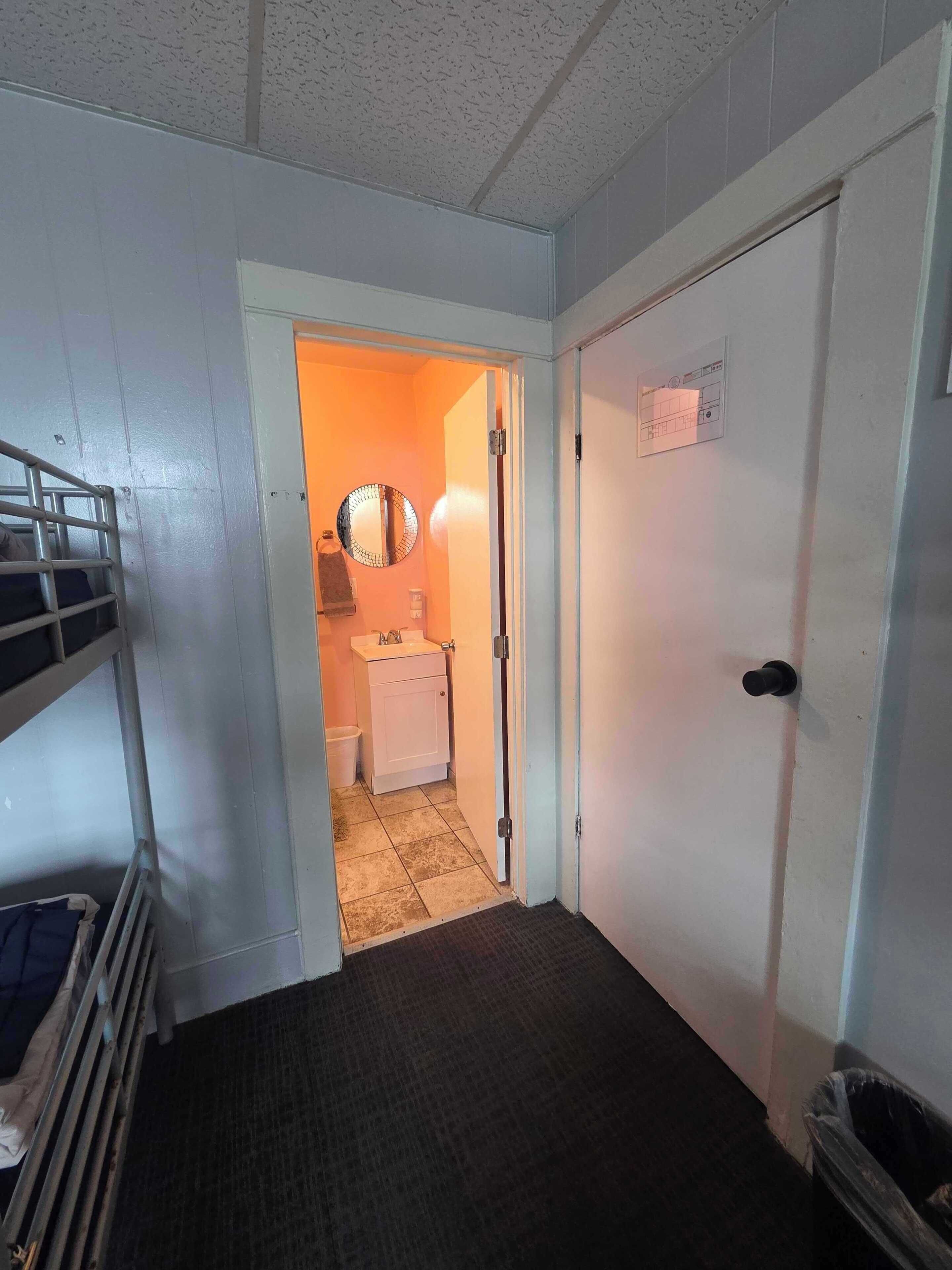 A narrow hallway with a bunk bed on the left, a door with a nameplate on the right, and a bathroom visible through the doorway.