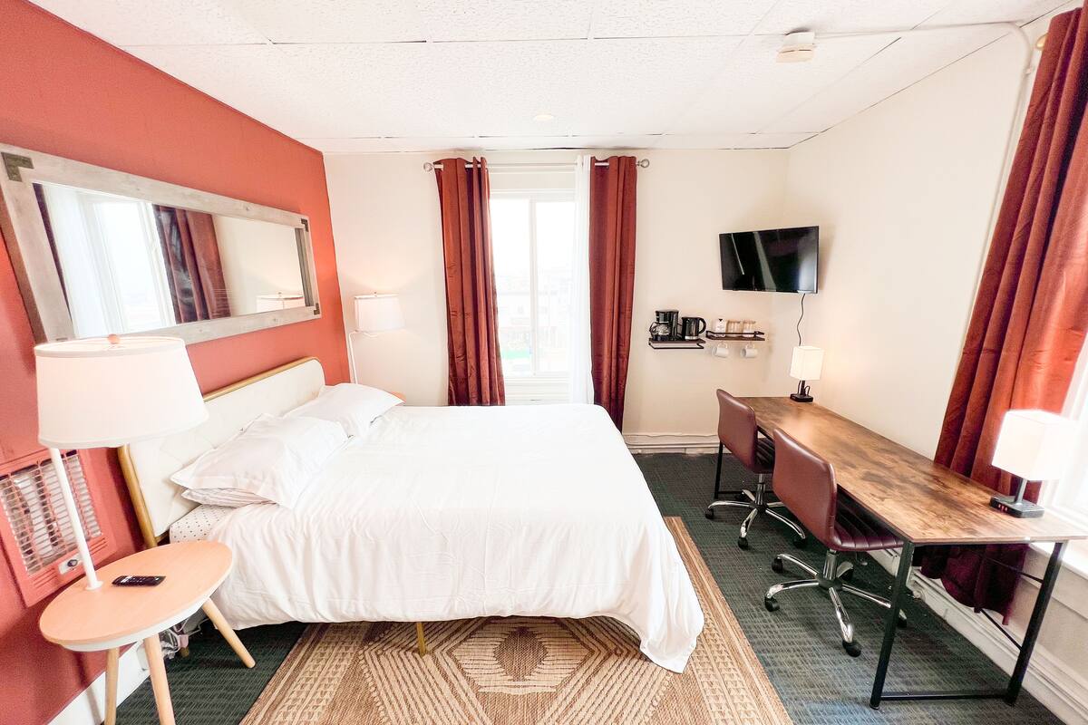 Une chambre d’hôtel équipée d’un lit, d’un bureau, d’une chaise, d’une télévision et d’une petite table avec une lampe.