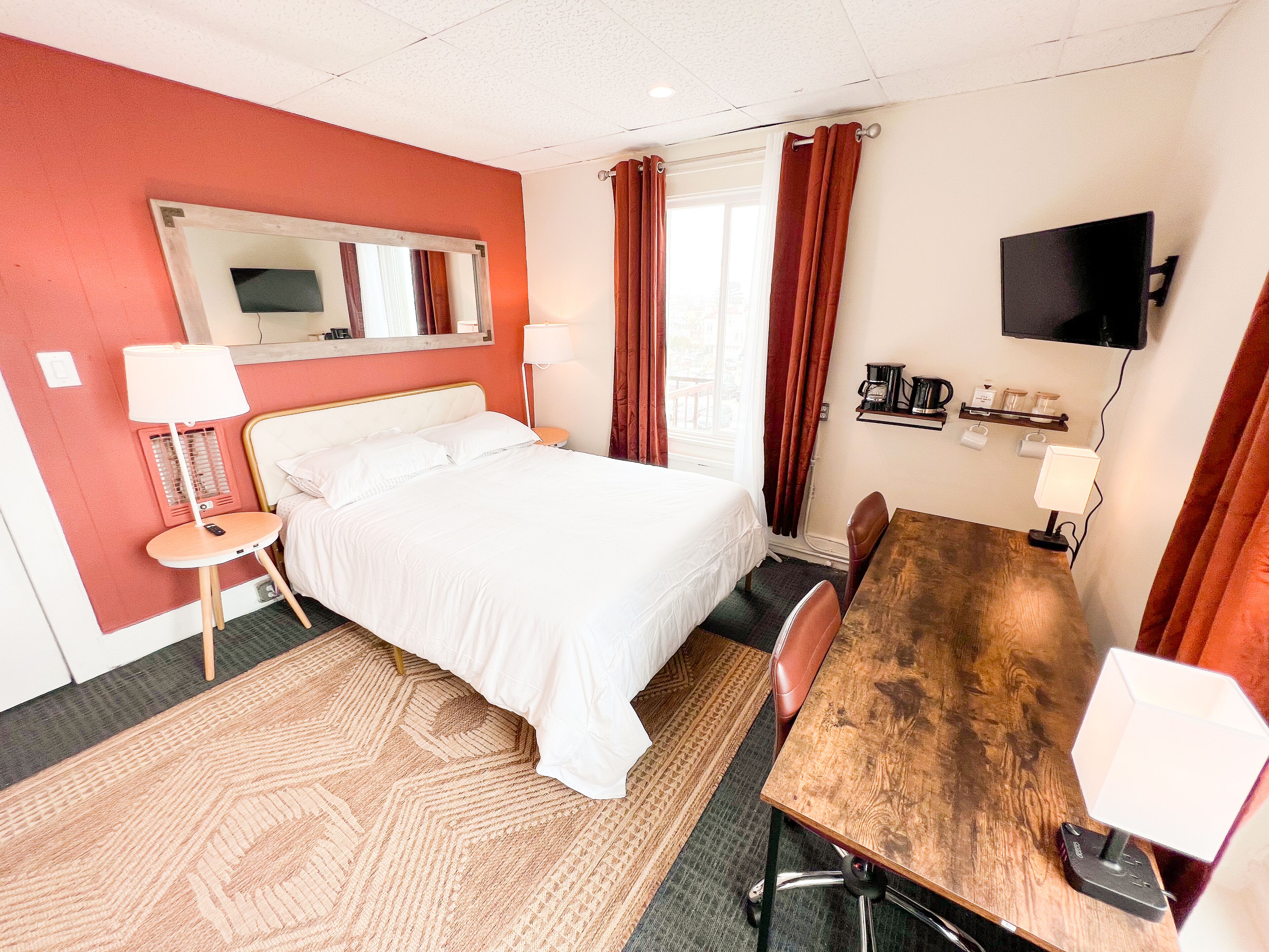 A hotel room with a bed, a desk, a chair, a TV, and a window with curtains.