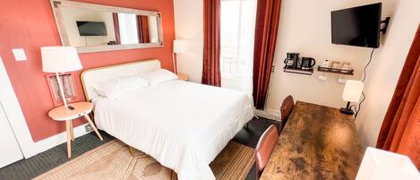 A hotel room with a bed, a desk, a chair, a TV, and a window with curtains.